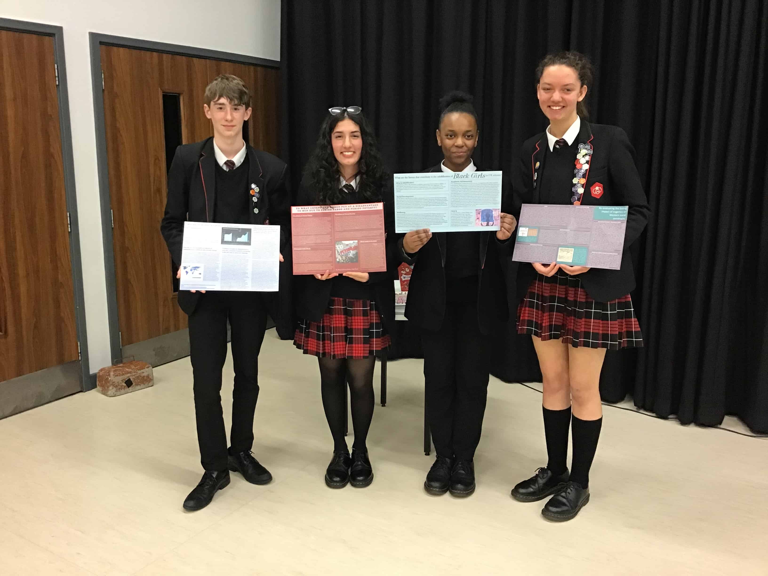 Four students from Didsbury High School hold their Apertura research posters at Cheadle Hulme High School.