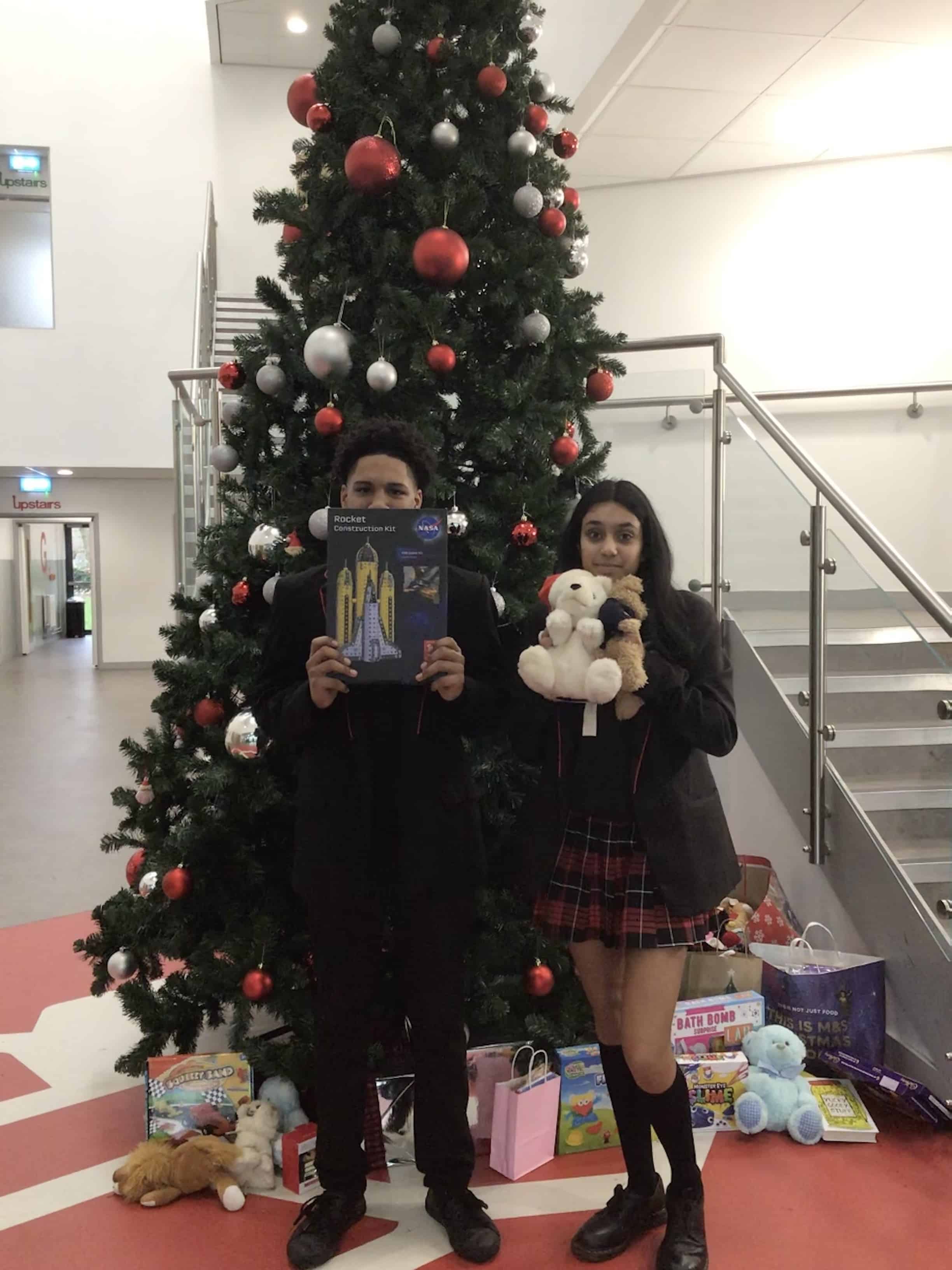 Head Prefects Twalha and Mya stand in front of the Christmas tree at Didsbury High School holding items donated by the school community for Mission Christmas.