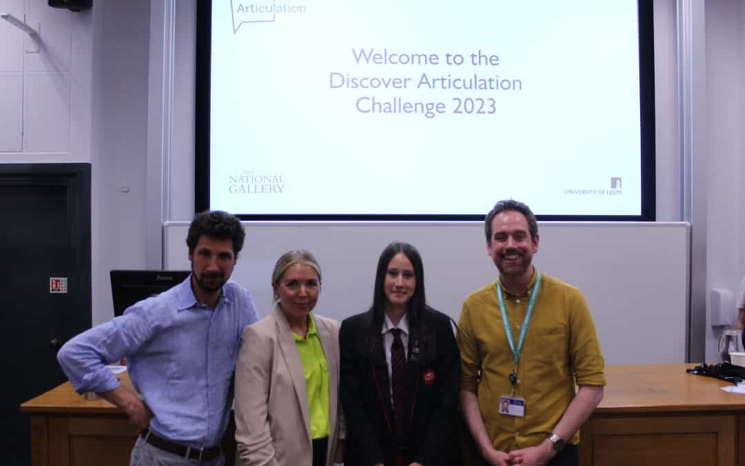 The judges of the Discover Articulation challenge, Mrs Patton (Lyla's art teacher) and Didsbury High School student Lyla stand together smiling in front of a projector screen which reads: "Welcome to the Discover Articulation Challenge 2023"