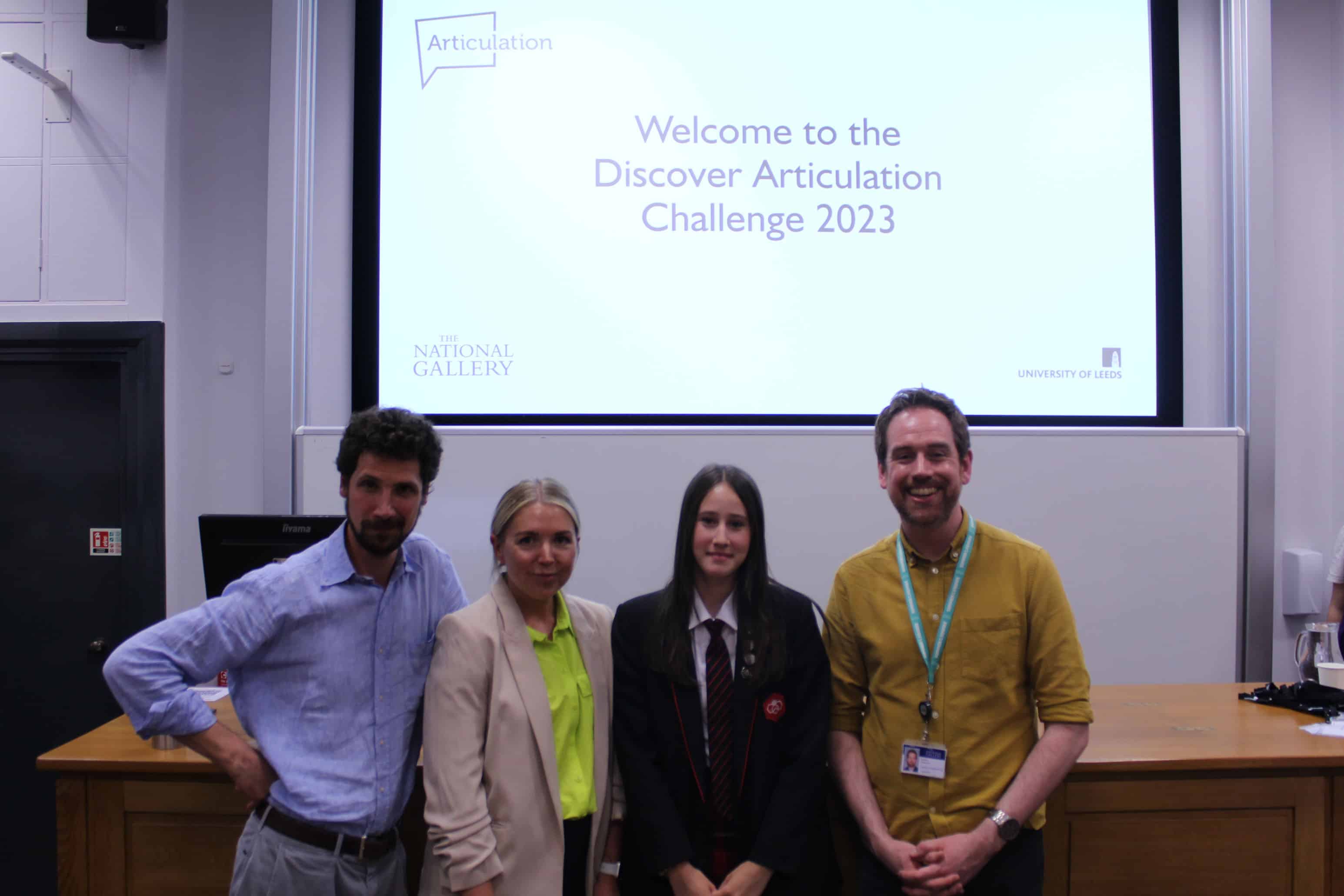 The judges of the Discover Articulation challenge, Mrs Patton (Lyla's art teacher) and Didsbury High School student Lyla stand together smiling in front of a projector screen which reads: "Welcome to the Discover Articulation Challenge 2023"